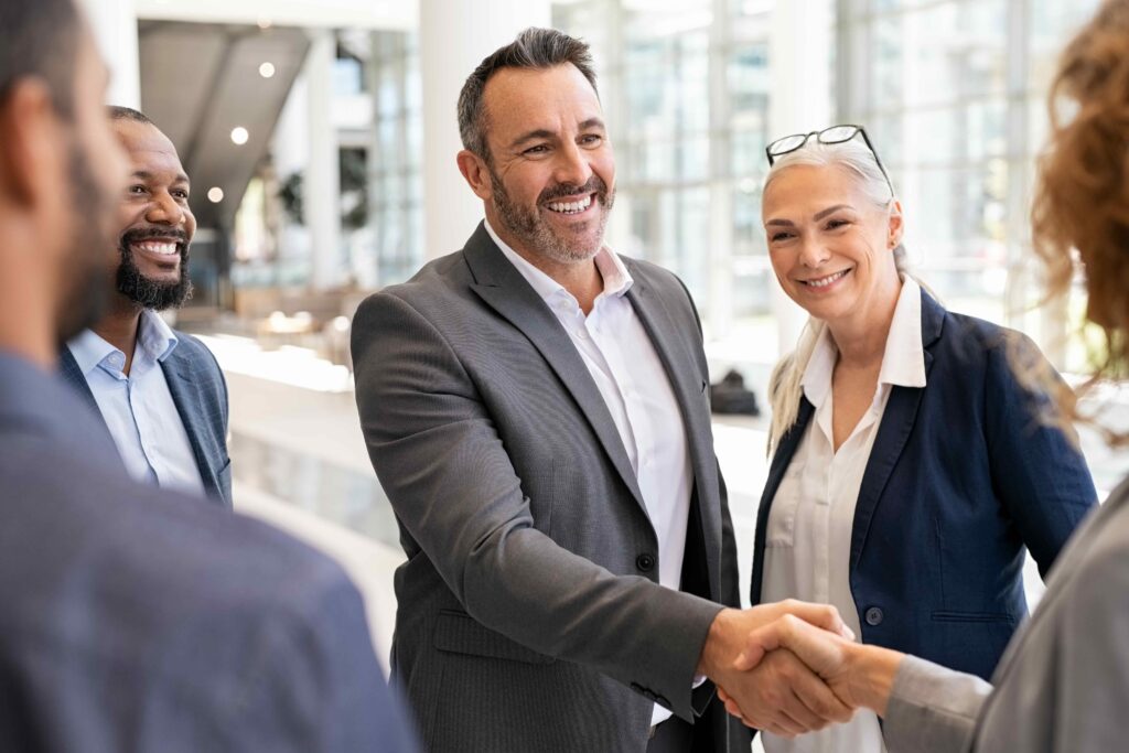 Smiling business colleagues shake hands in a bright, modern office lobby.